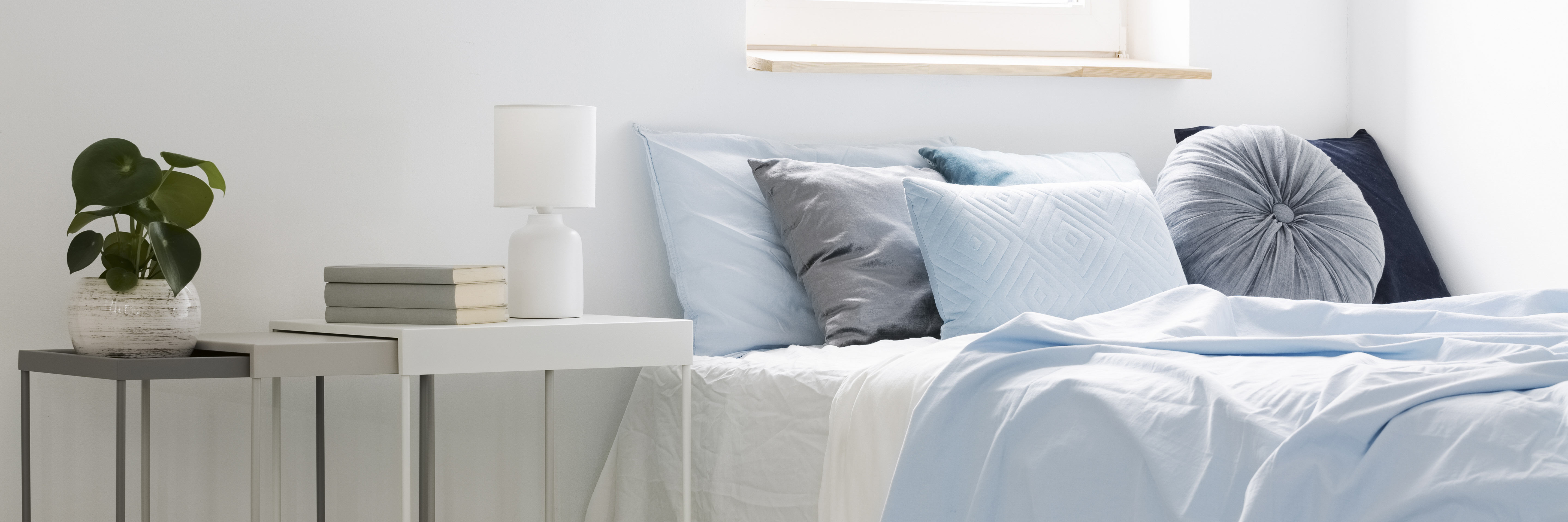 bed-with-blue-bedding-and-cushions-standing-next-to-white-tables-with-books